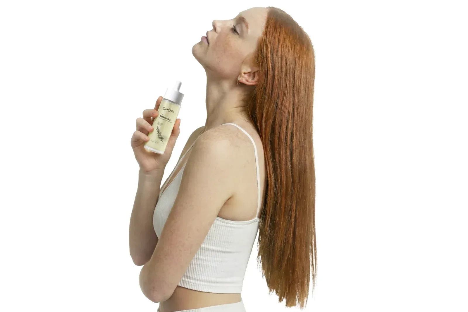 Red-haired model holding the Ghori® Rosemary Mint & Biotin Oil beside her long, glossy hair